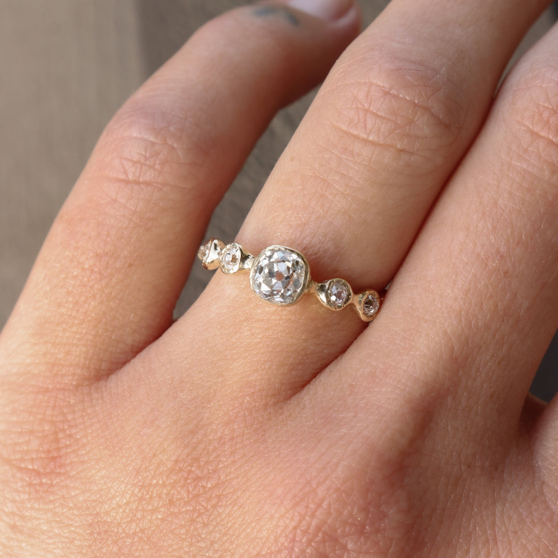 Close-up of a hand wearing a diamond ring with a beige background