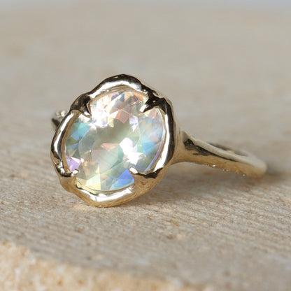 Gold ring with a large, faceted gemstone on a beige background
