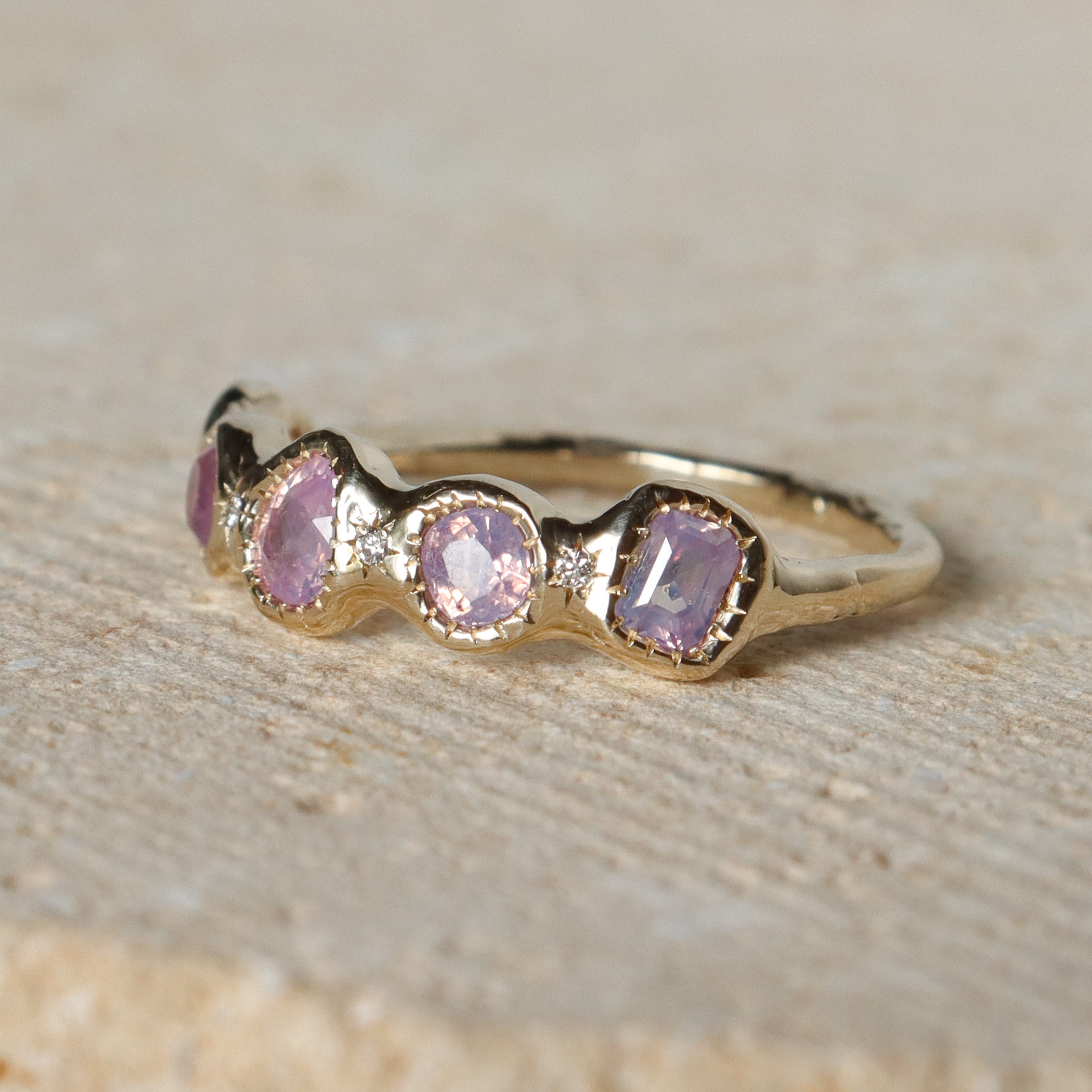 Gold ring with pink gemstones on a textured beige surface