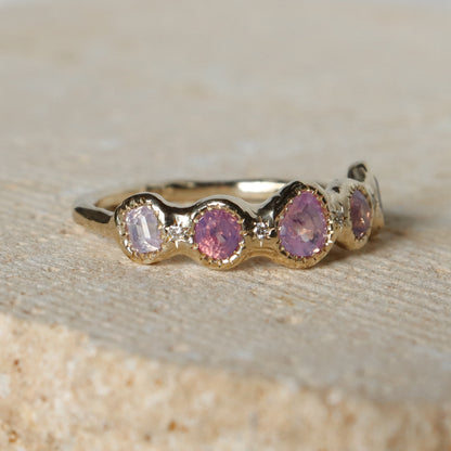 Gold ring with pink gemstones on a textured beige surface