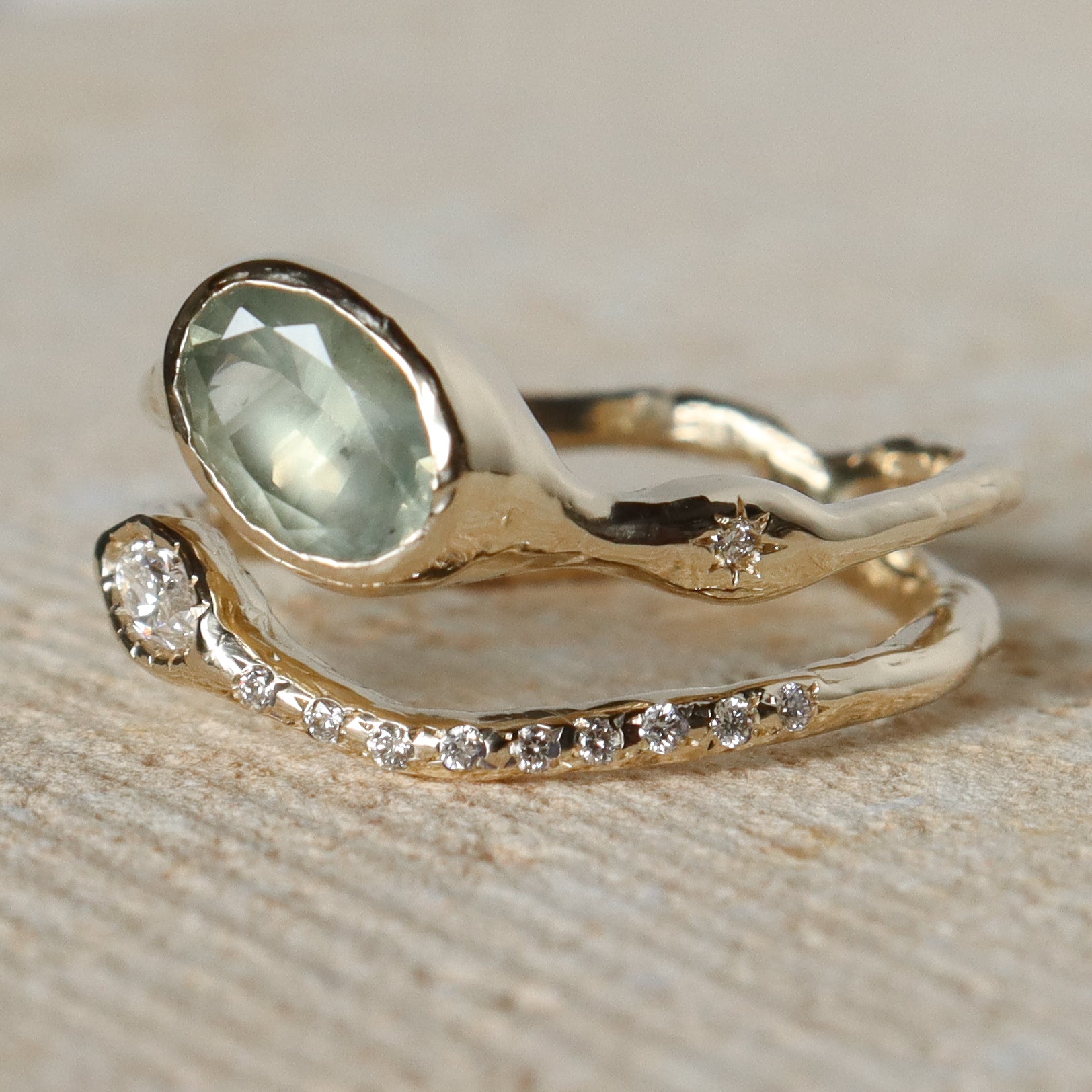 Gold ring with green gemstone and diamond-studded band on a textured surface