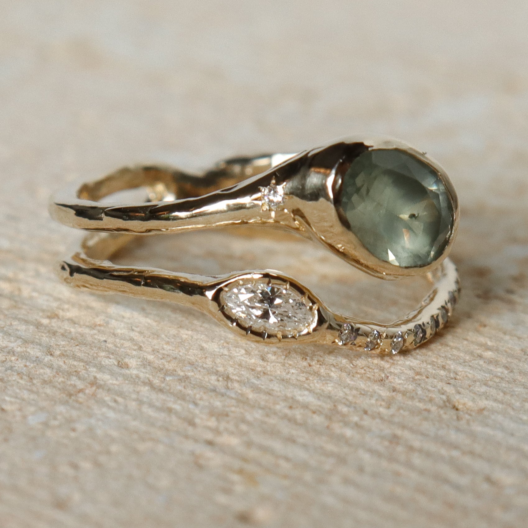 Gold ring with green gemstone and diamond on a beige surface