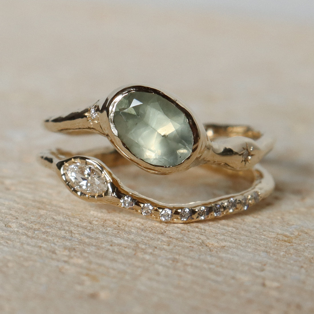 Gold ring with green gemstone and smaller diamond on a stone surface