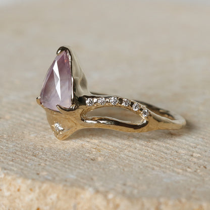 Gold ring with a pink gemstone on a beige surface