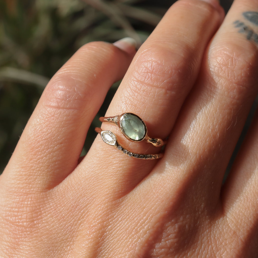 Hand wearing a ring with a green stone against a natural background