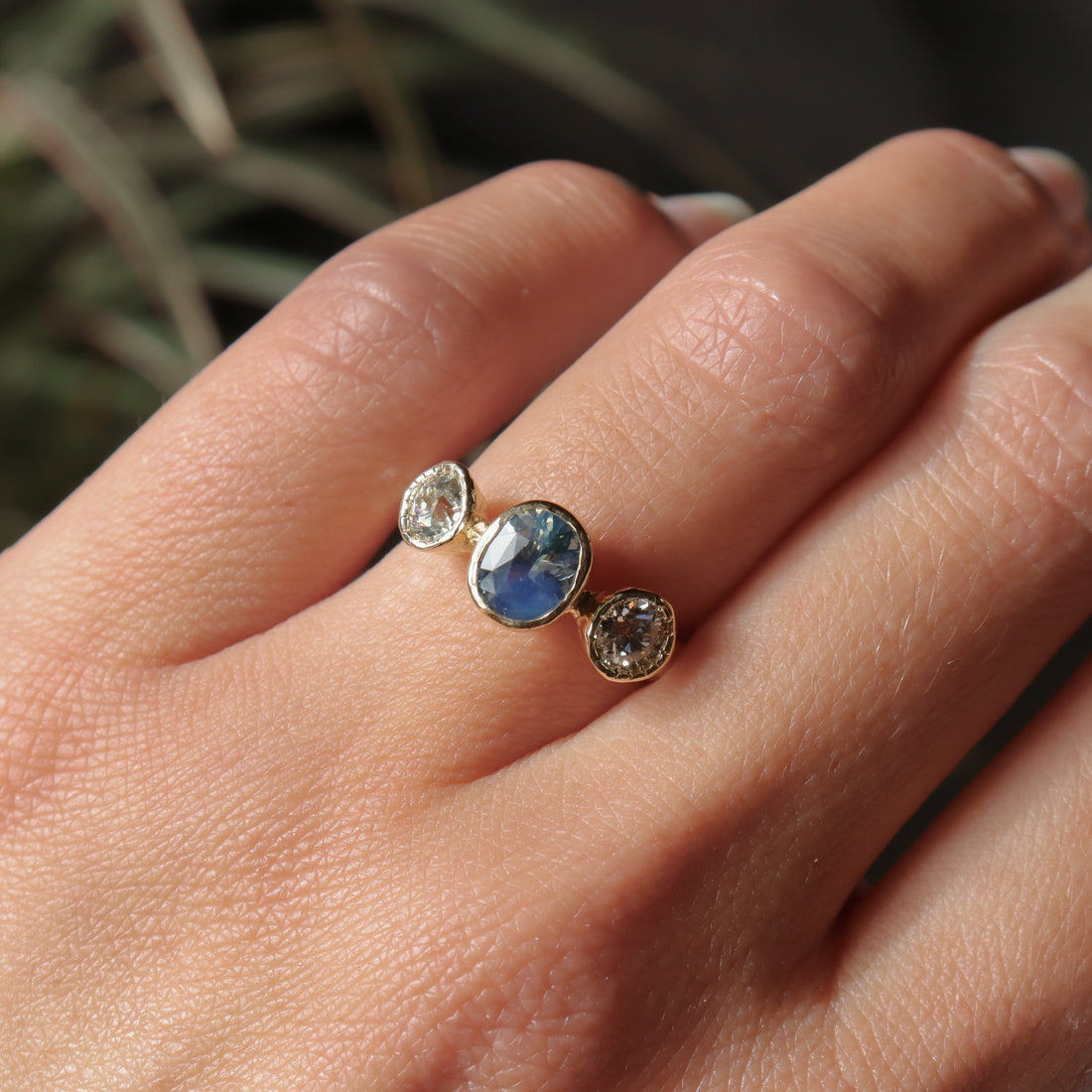 Gold ring with three gemstones on a hand against a blurred natural background