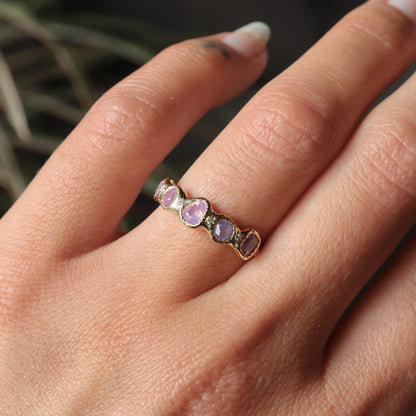 Close-up of a hand wearing a ring with pink gemstones against a blurred background
