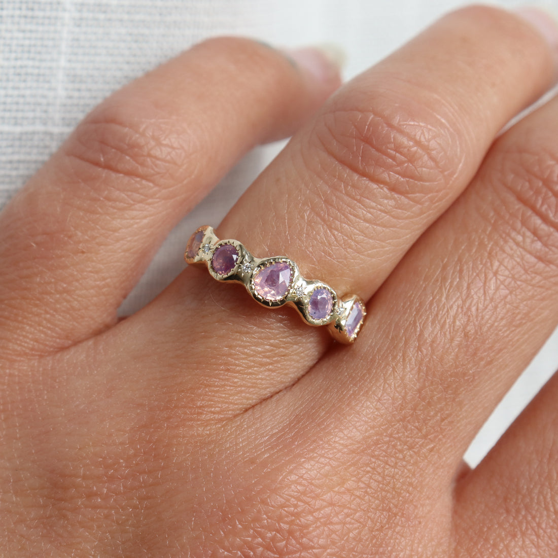 Close-up of a hand wearing a ring with pink gemstones on a neutral background