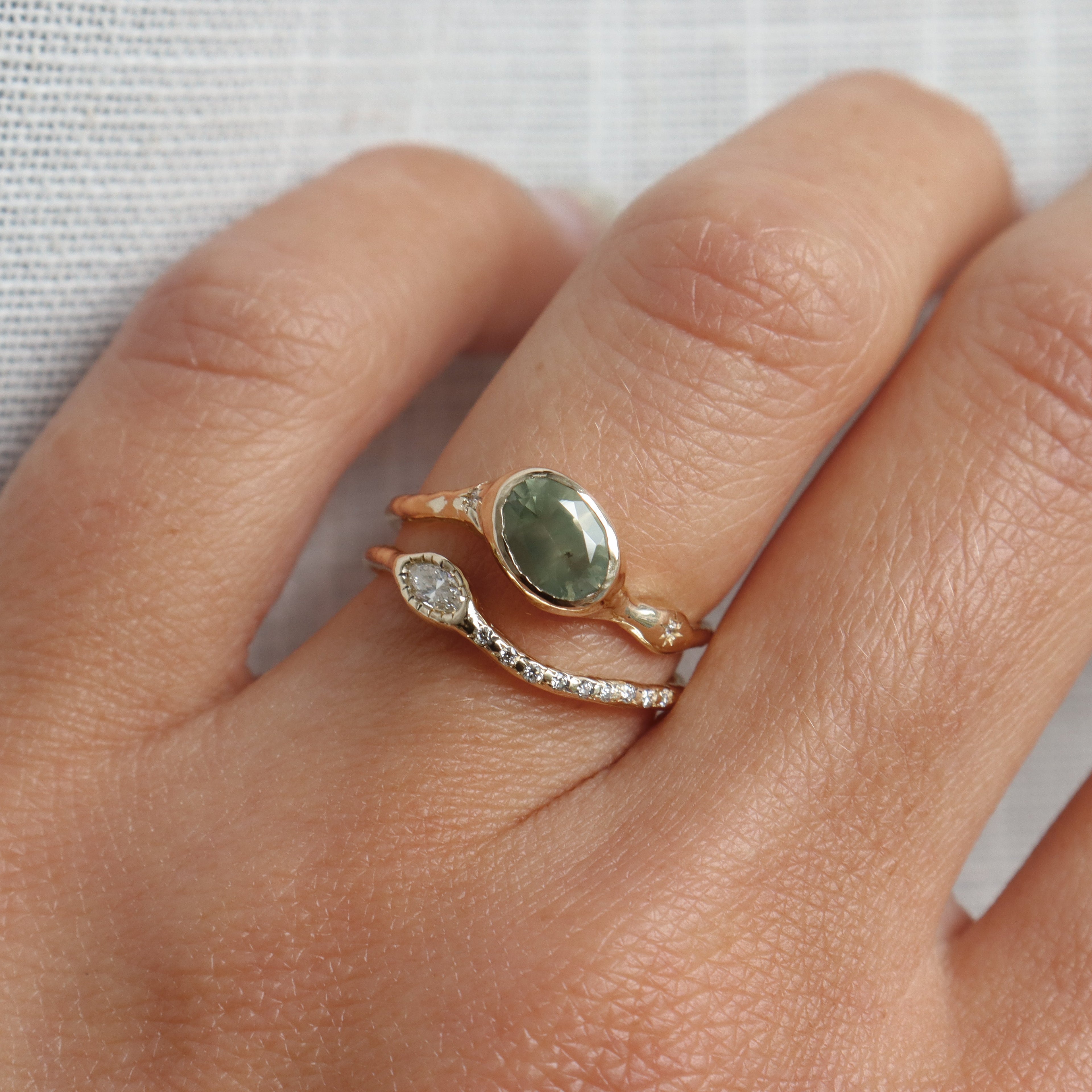 Close-up of a hand wearing a gold ring with a green stone on a light background
