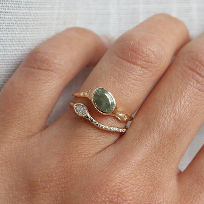 Close-up of a hand wearing a gold ring with a green stone on a light background