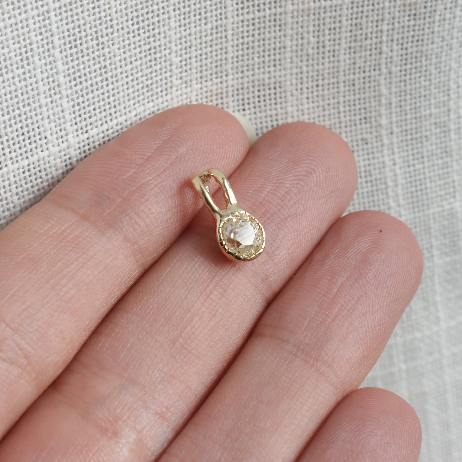Gold pendant with a clear gemstone held between fingers on a light fabric background