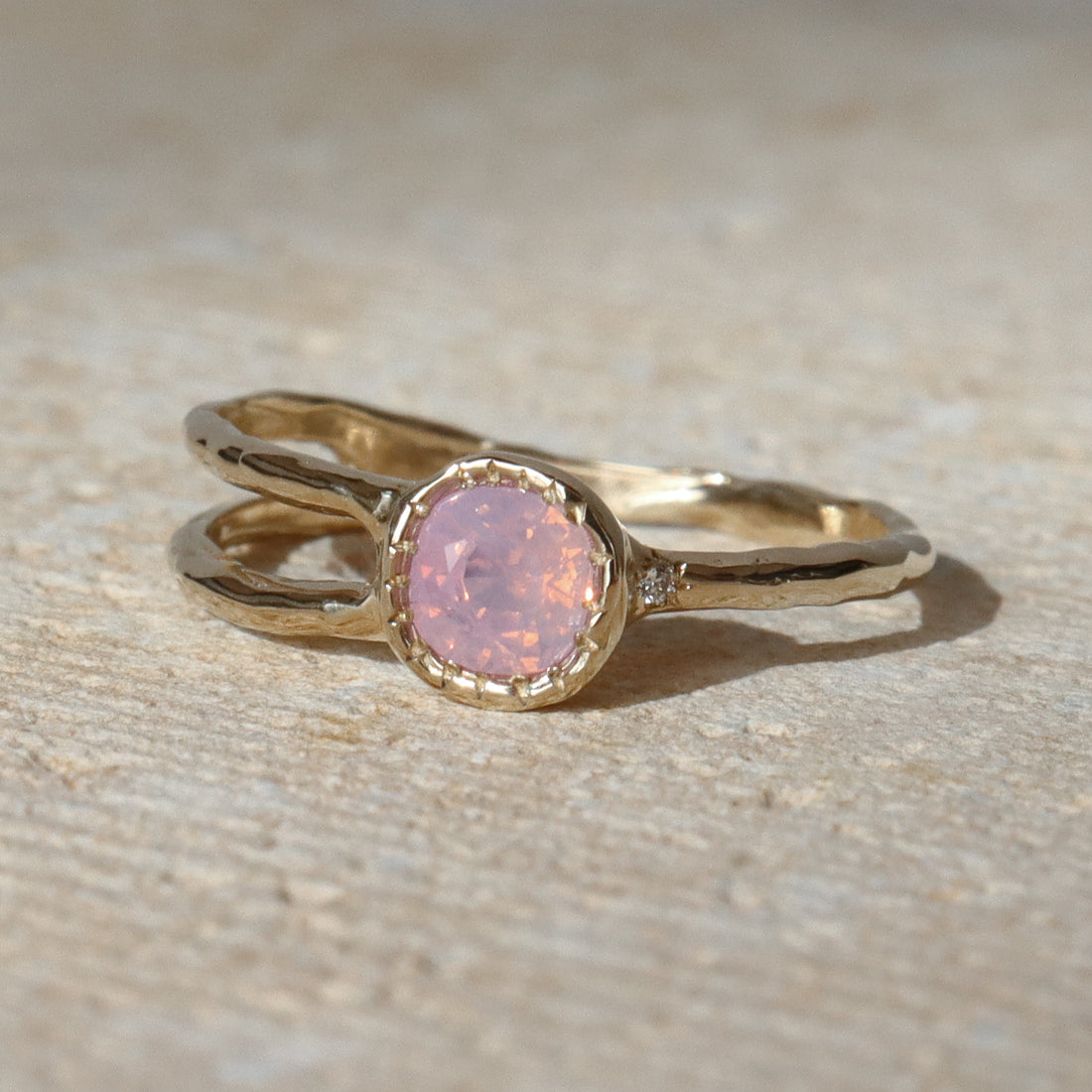 Gold ring with a pink gemstone on a beige surface