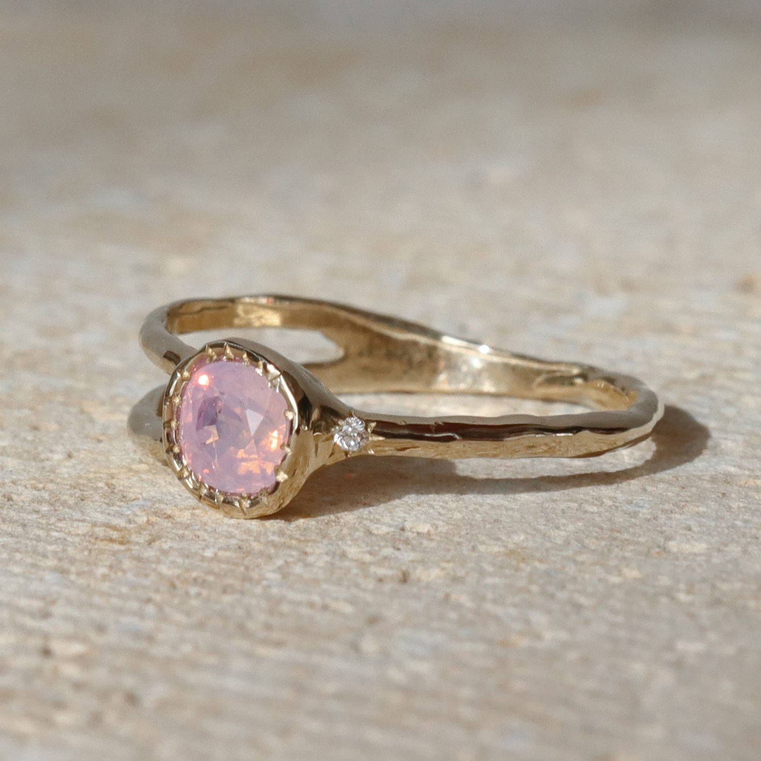 Gold ring with a pink gemstone on a textured beige surface