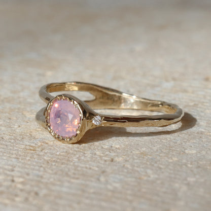 Gold ring with a pink gemstone on a textured beige surface