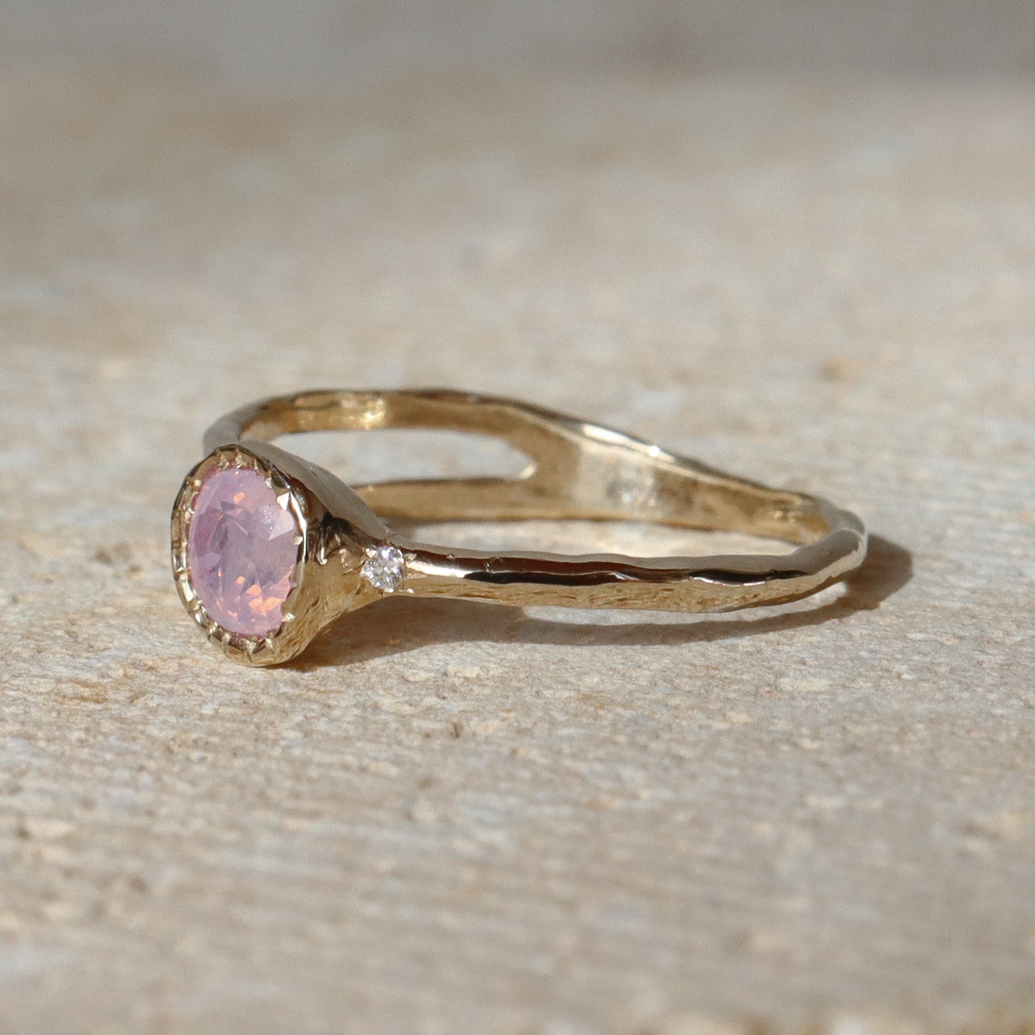 Gold ring with a pink gemstone on a beige surface