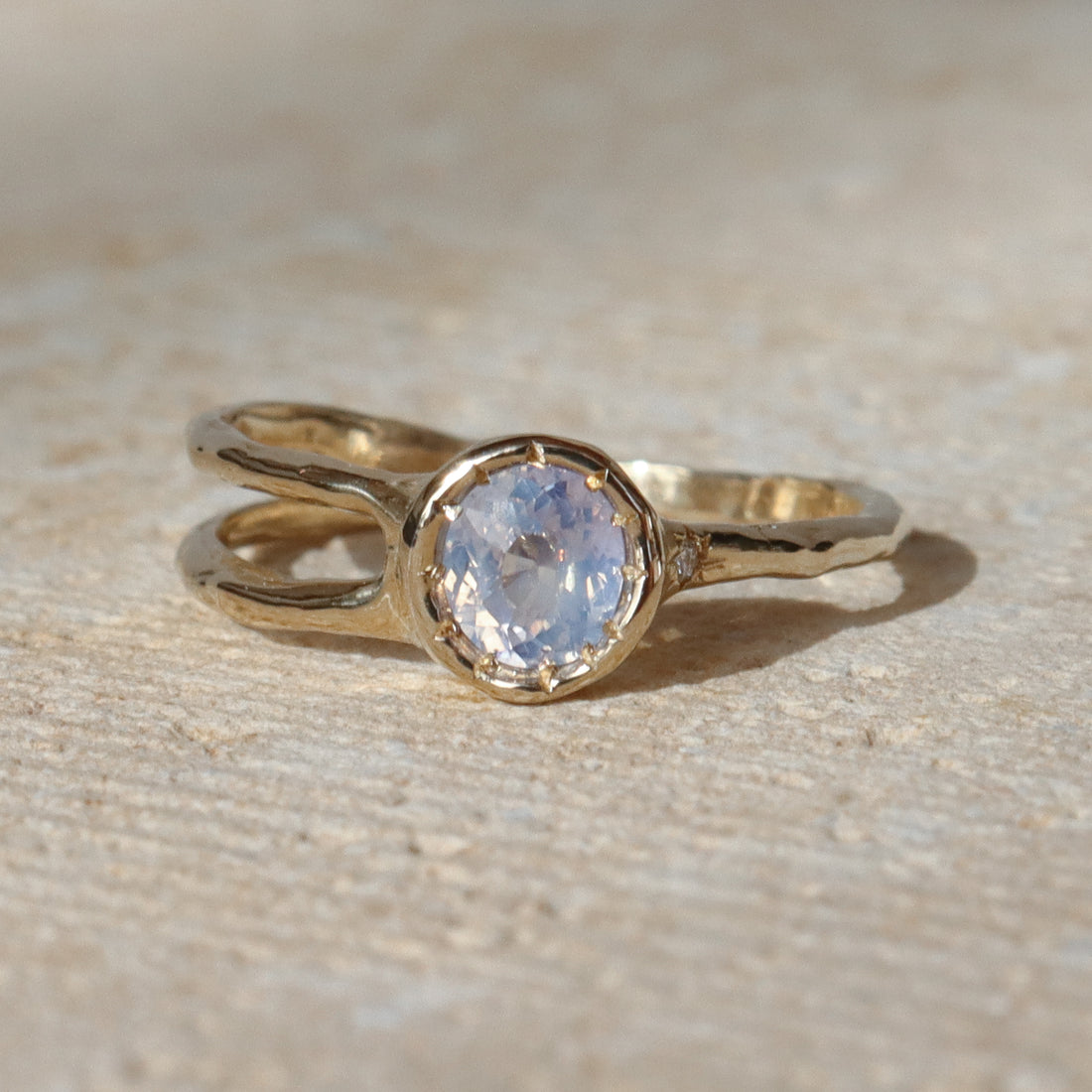 Gold ring with a central gemstone on a textured beige surface