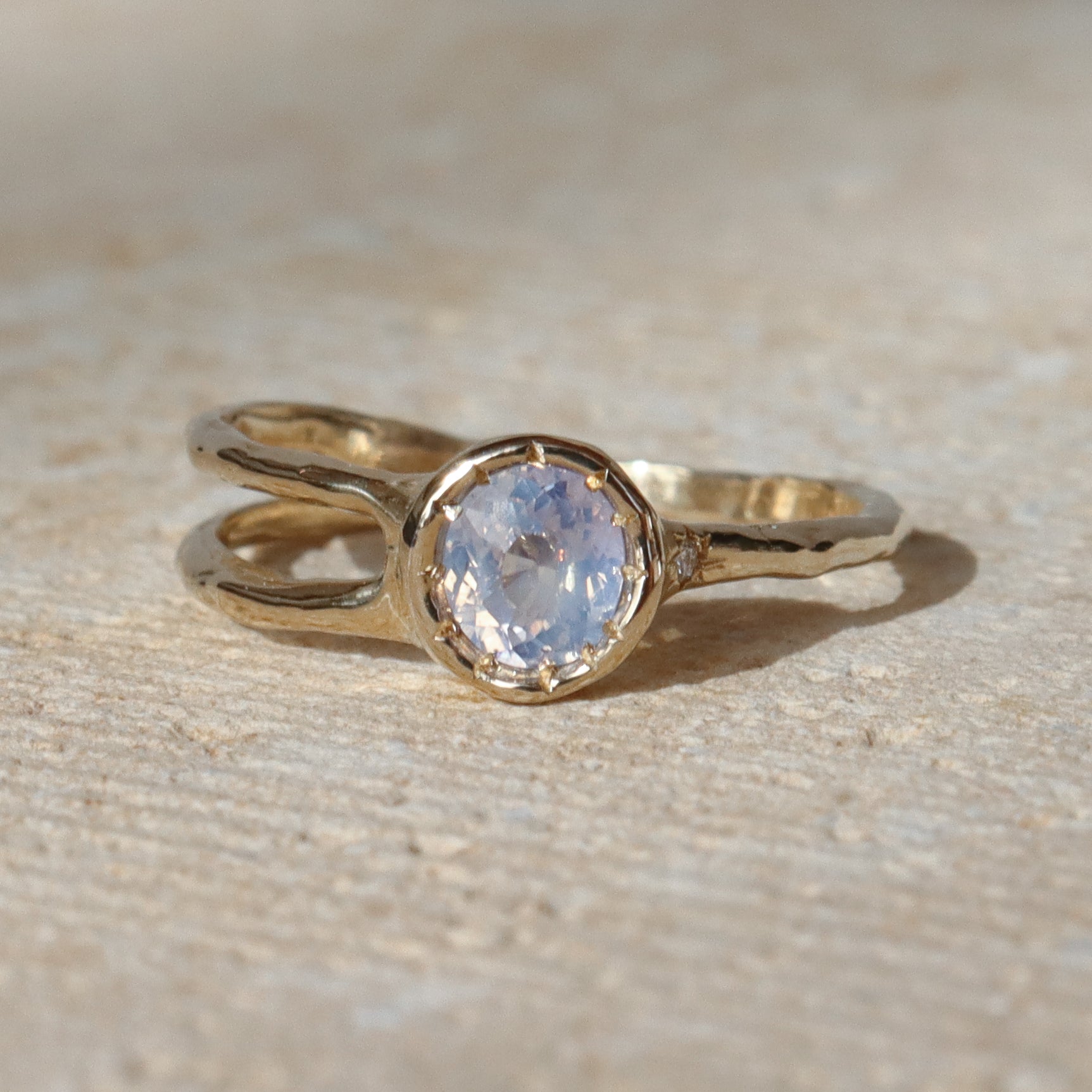 Gold ring with a central gemstone on a textured beige surface