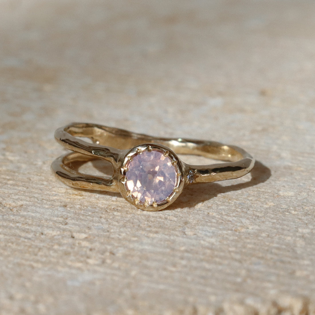 Gold ring with a pink gemstone on a beige surface