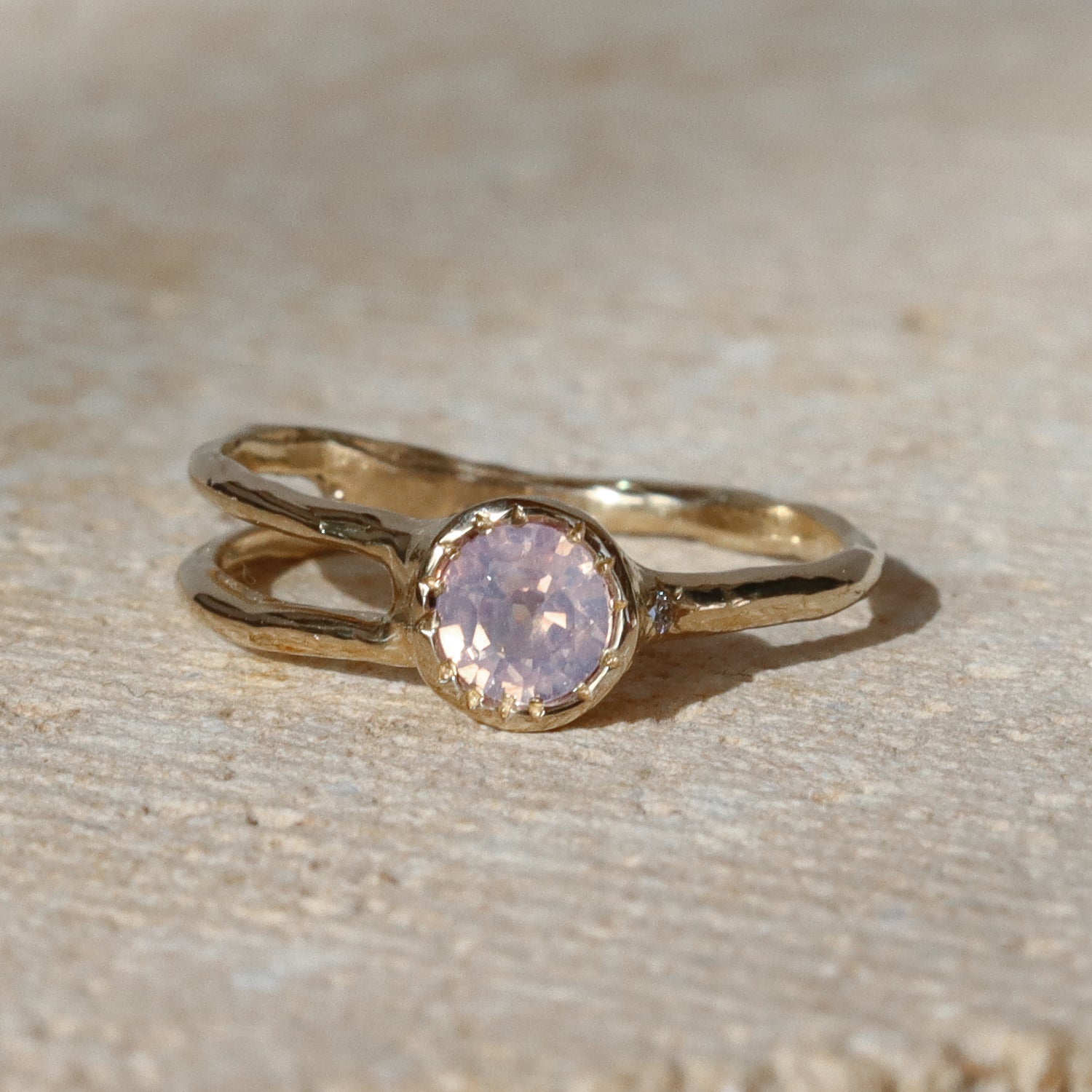 Gold ring with a pink gemstone on a beige surface