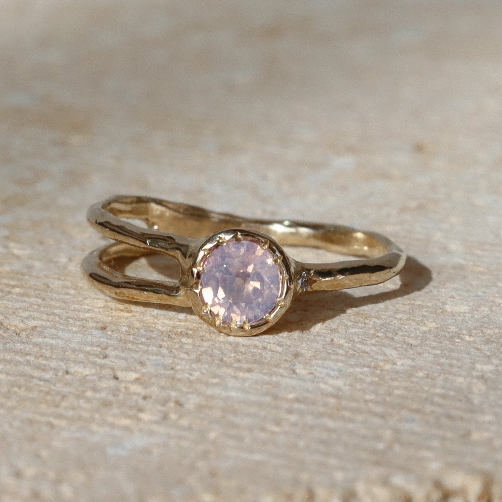 Gold ring with a pink gemstone on a beige surface