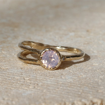 Gold ring with a pink gemstone on a beige surface