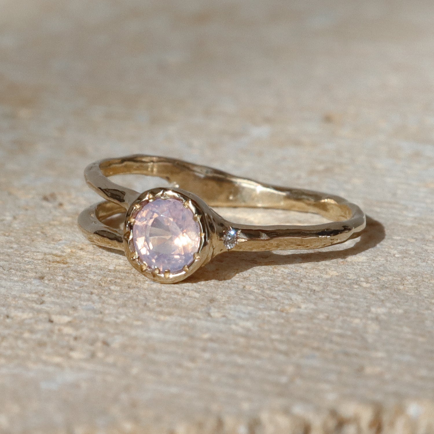 Gold ring with a pink gemstone on a beige surface