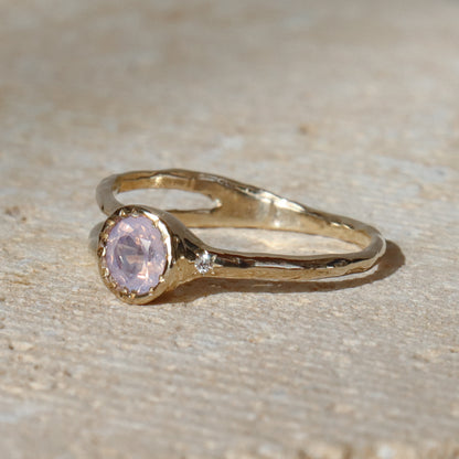 Gold ring with a pink gemstone on a beige surface