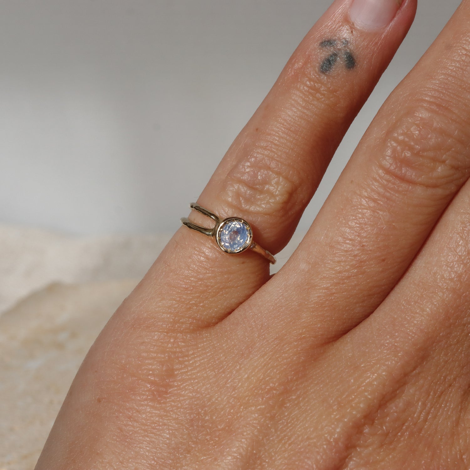 Close-up of a hand wearing a gold ring with a gemstone on a neutral background