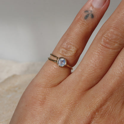 Close-up of a hand wearing a gold ring with a gemstone on a neutral background