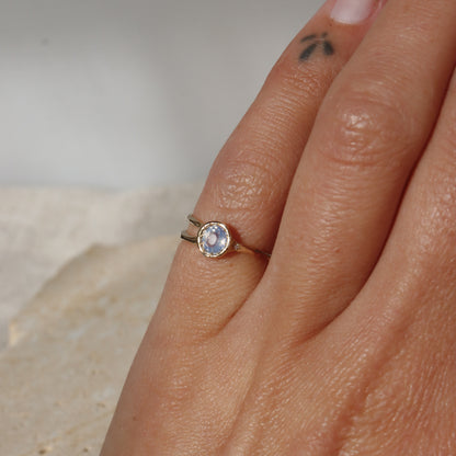 Close-up of a hand wearing a gold ring with a blue gemstone on a neutral background