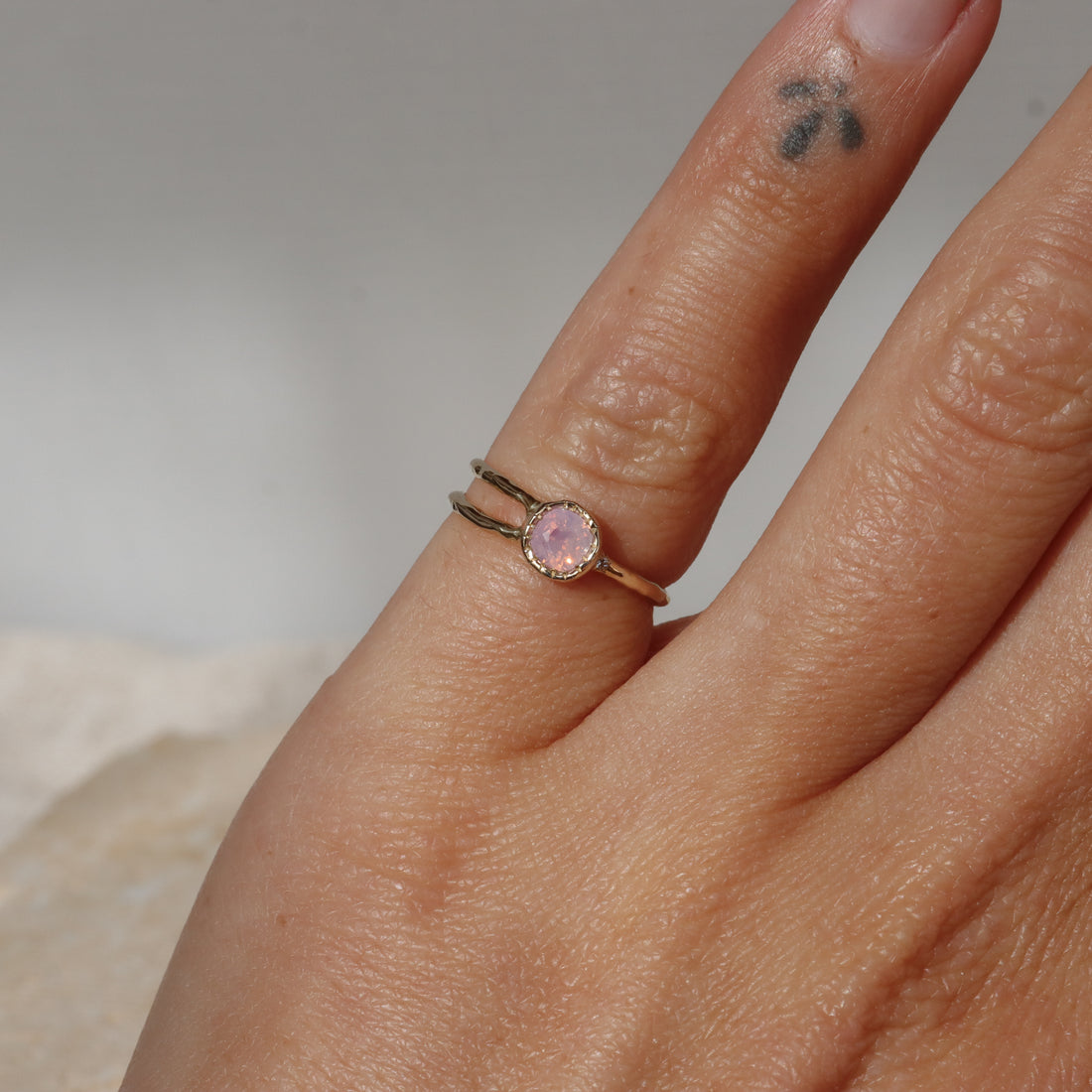 Hand wearing a ring with a pink gemstone on a neutral background