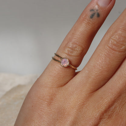 Hand wearing a ring with a pink gemstone on a neutral background