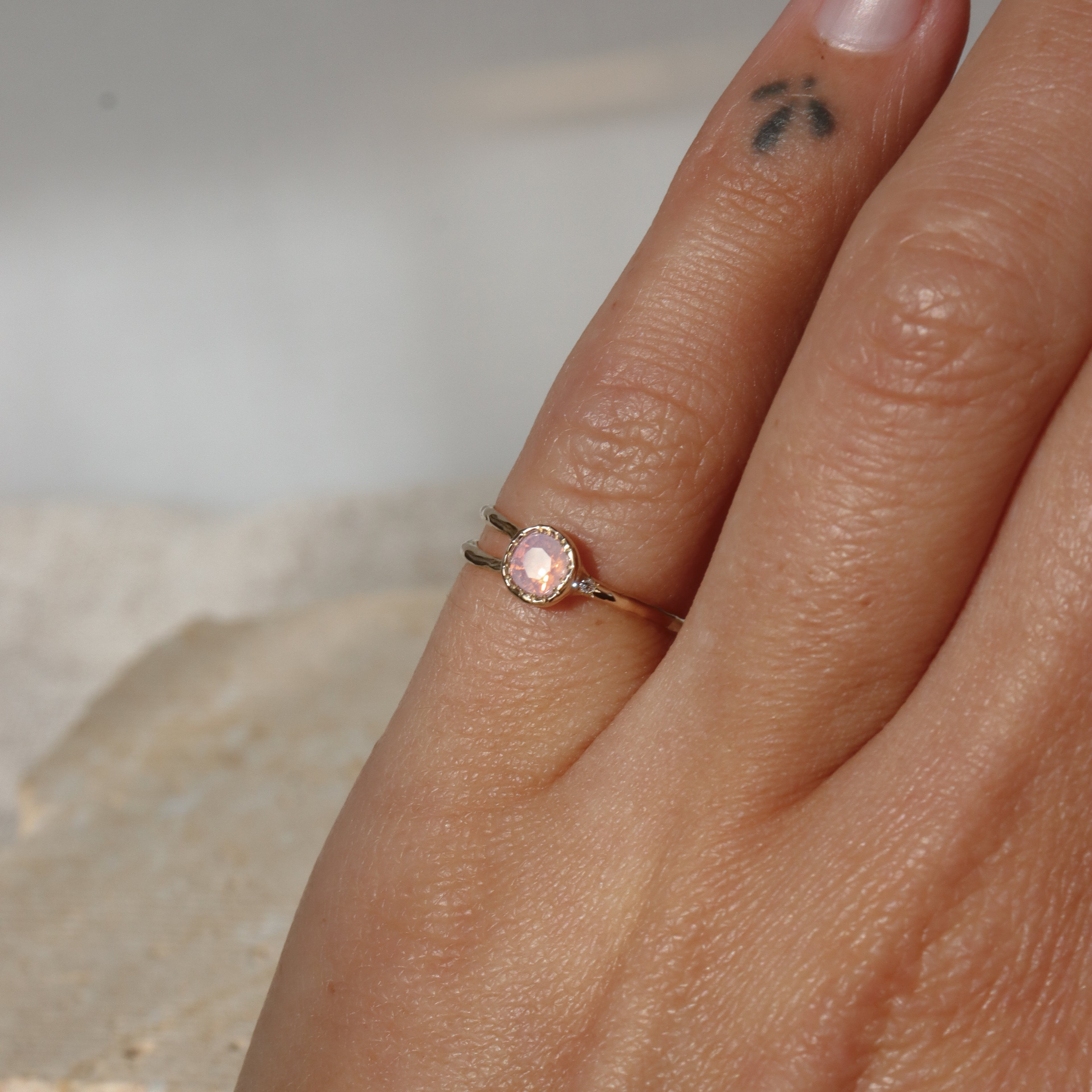 Close-up of a hand wearing a ring with a pink gemstone on a neutral background