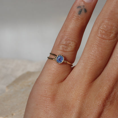 Hand wearing a gold ring with a blue gemstone on a neutral background