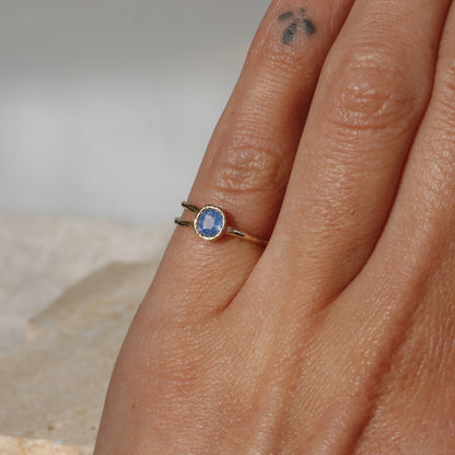 Close-up of a hand wearing a gold ring with a blue gemstone on a neutral background