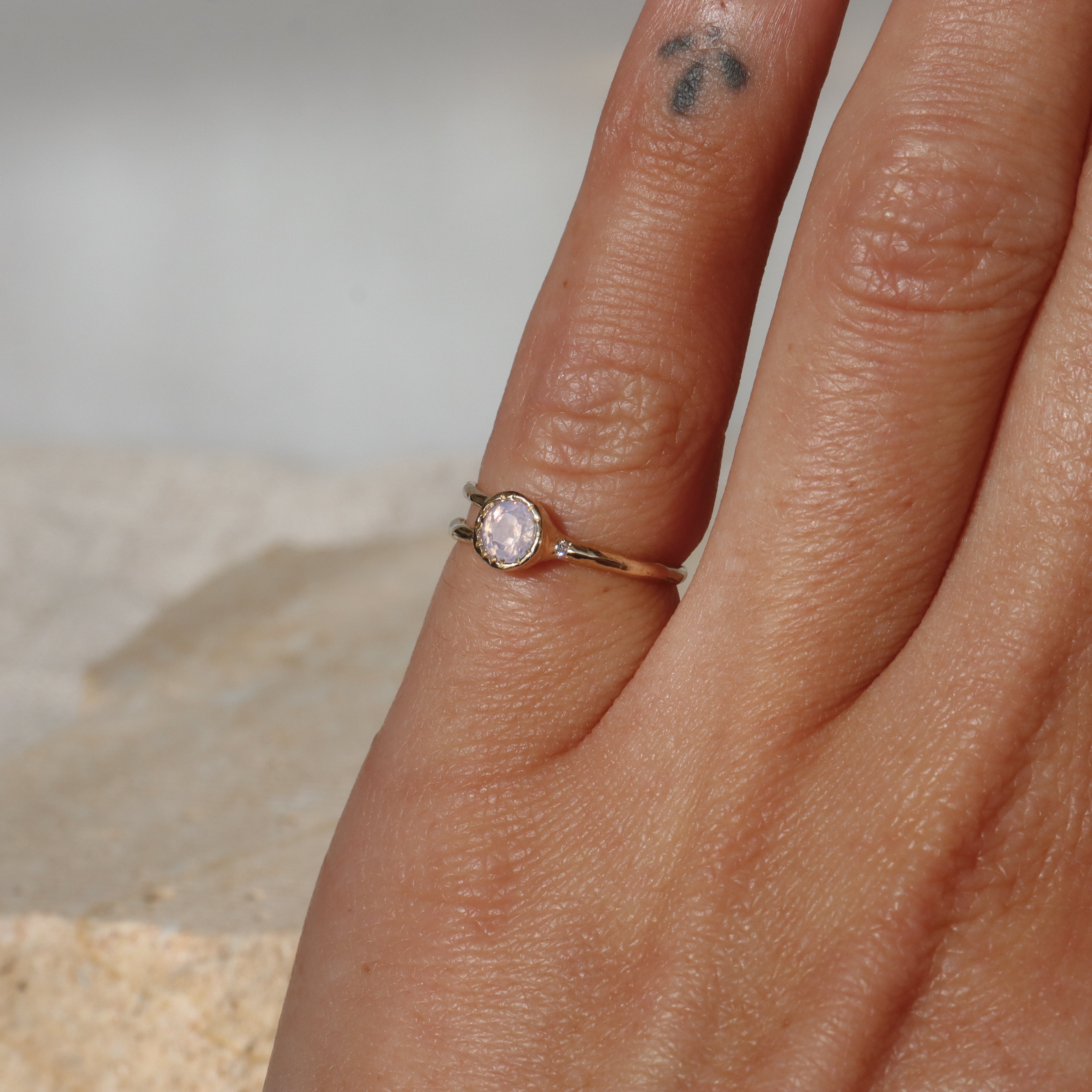 Close-up of a hand wearing a gold ring with a diamond on a neutral background