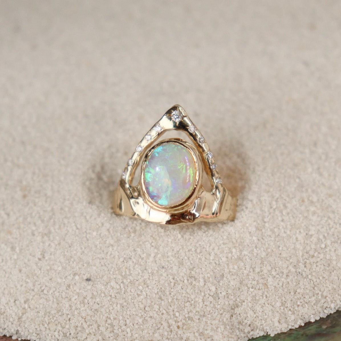 Stunning ring featuring a bezel-set opal on a wide, organically shaped band, adorned with a crown-like V-shaped band encircling the opal and embellished with glistening diamond accents
