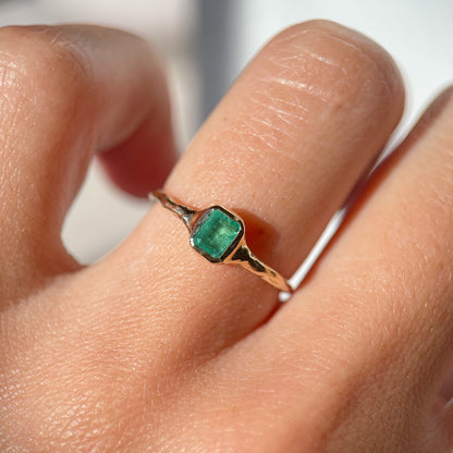 Mini emerald ring elegantly worn on a finger, showcasing its vibrant green gemstone and delicate gold band.