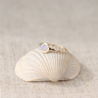 A round opal ring, set on a slender band with small tick-like accents that radiate like a starburst, creating a mesmerizing and celestial jewelry piece.