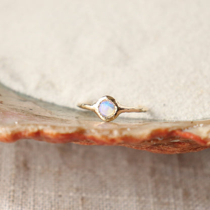 A round opal ring, set on a slender band with small tick-like accents that radiate like a starburst, creating a mesmerizing and celestial jewelry piece.