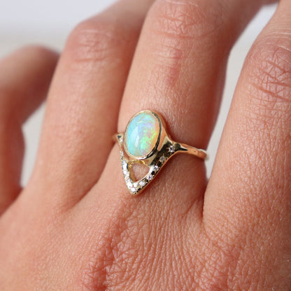Elegant opal ring featuring a V-shaped design adorned with sparkling diamond accents, shown on a finger for scale and a partial side view