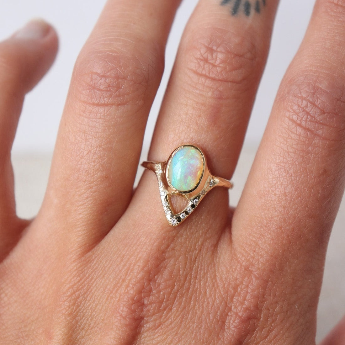 Elegant opal ring featuring a V-shaped design adorned with sparkling diamond accents, shown on a finger for scale