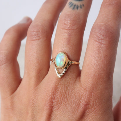 Elegant opal ring featuring a V-shaped design adorned with sparkling diamond accents, shown on a finger for scale.