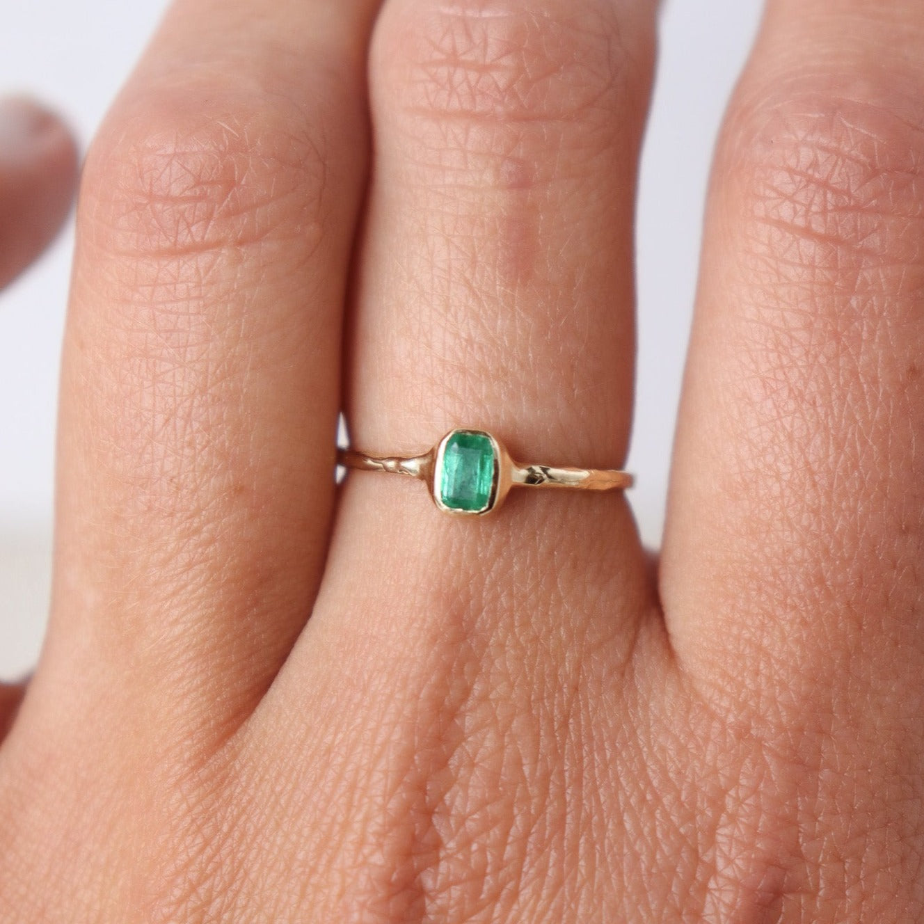 Mini emerald ring elegantly worn on a finger, showcasing its vibrant green gemstone and delicate gold band