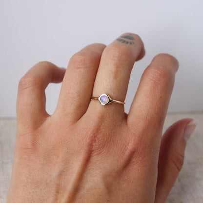 A round opal ring, set on a slender band with small tick-like accents that radiate like a starburst, creating a mesmerizing and celestial jewelry piece. Worn on a hand to show scale.