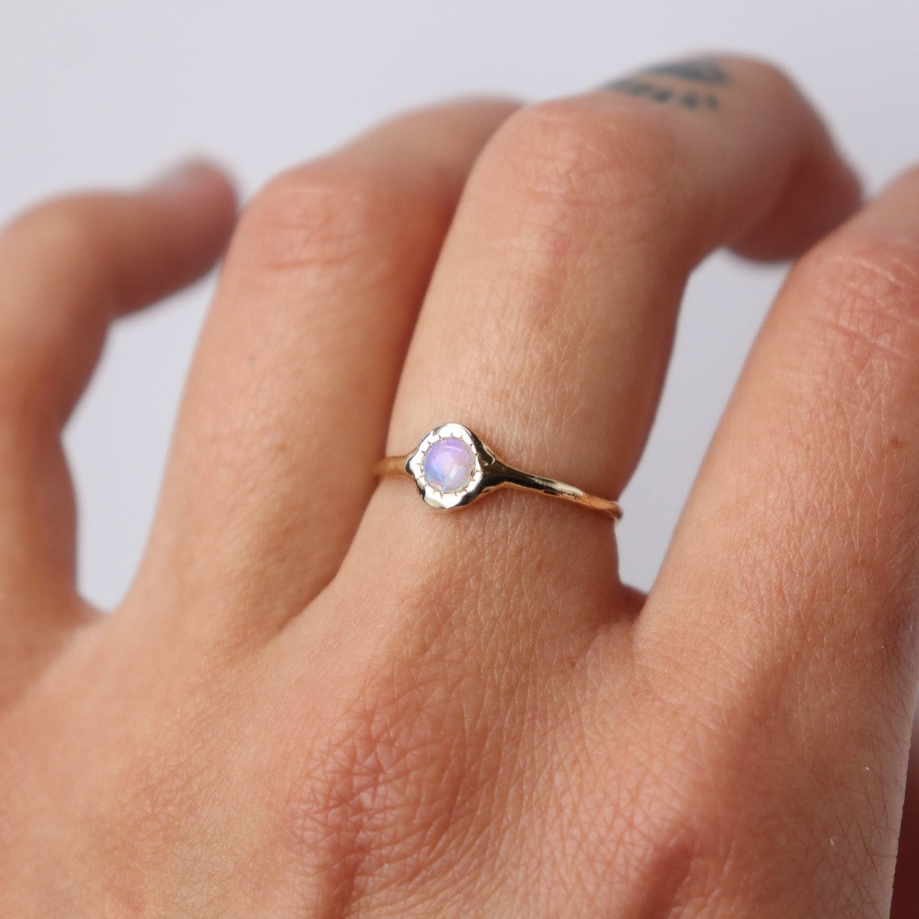 Unique round opal ring, set on a slender band with small tick-like accents that radiate like a starburst, creating a mesmerizing and celestial jewelry piece, worn on a hand to showcase scale.
