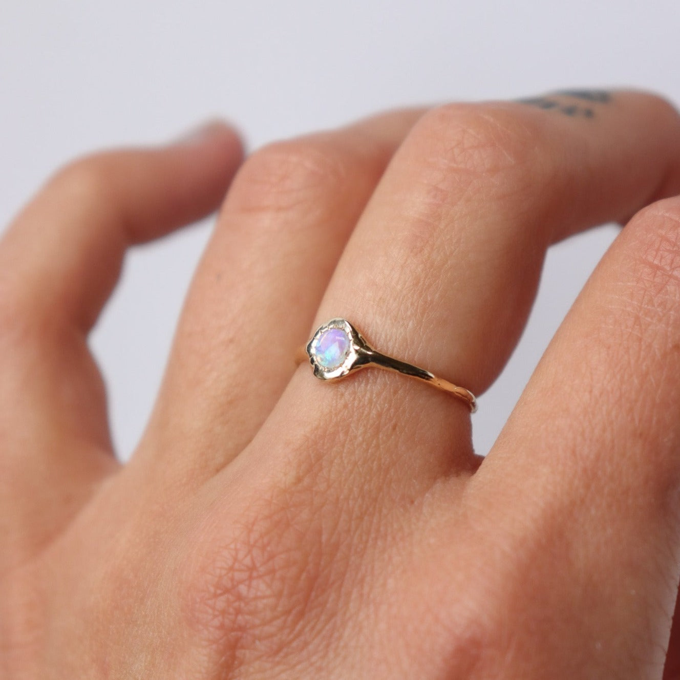 A round opal ring, set on a slender band with small tick-like accents that radiate like a starburst, creating a mesmerizing and celestial jewelry piece, worn on a hand to show scale.