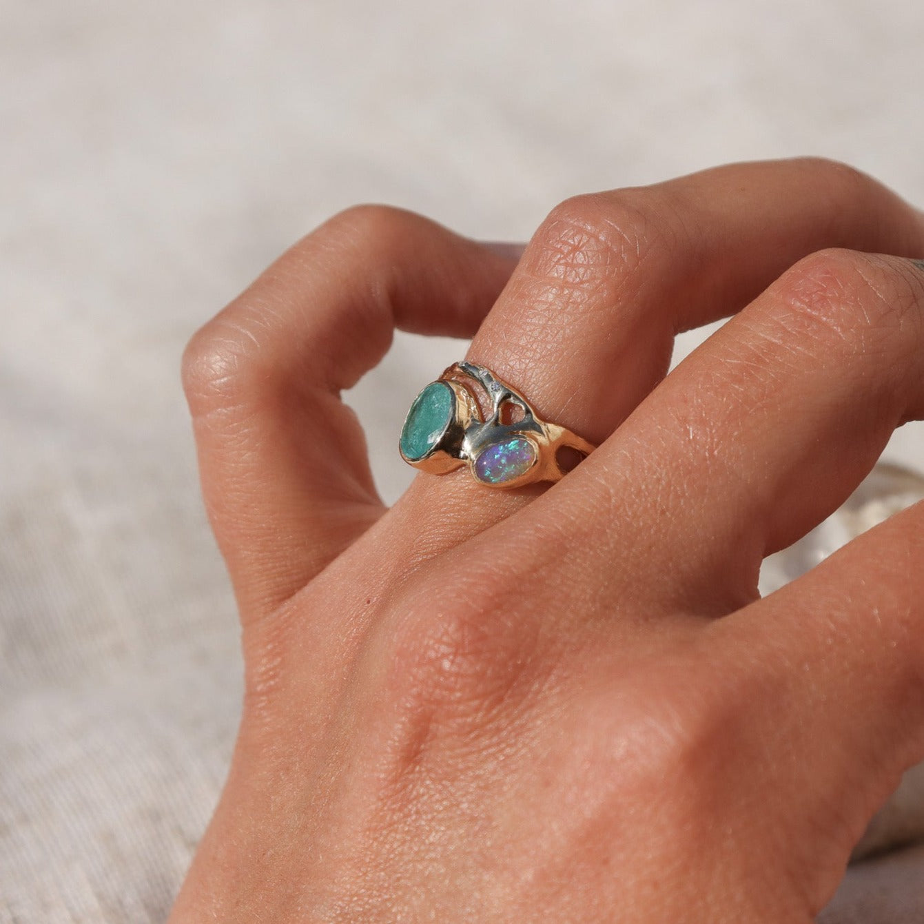 Organically shaped ring with a stunning Paraiba tourmaline and opal, bezel-set and accented with dazzling diamonds worn on a finger and showing the side.