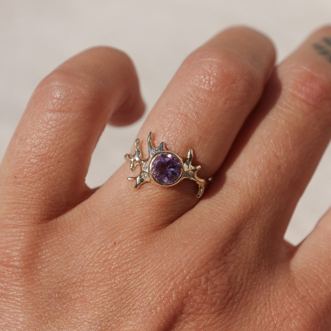Exquisite round brilliant cut ametrine gemstone, bezel-set in a gold band with an organic coral-like design, adorned with sparkling diamond accents, worn on a finger to show scale.