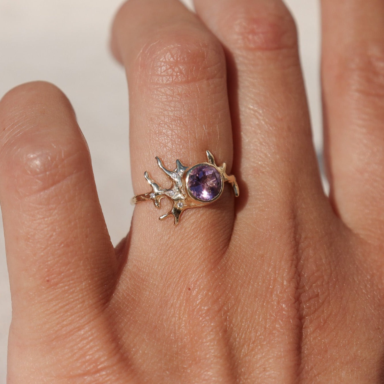 Exquisite round brilliant cut ametrine gemstone, bezel-set in a gold band with an organic coral-like design, adorned with sparkling diamond accents, shown on a  finger to depict scale.